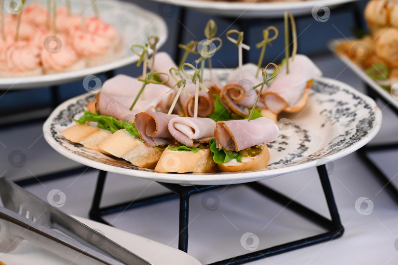 Скачать Разнообразная закуска для кейтеринга с канапе из ветчины и горчицей на багете для украшения мероприятия или вечеринки с вкусной пикантной мясной закуской на фуршетном столе фотосток Ozero