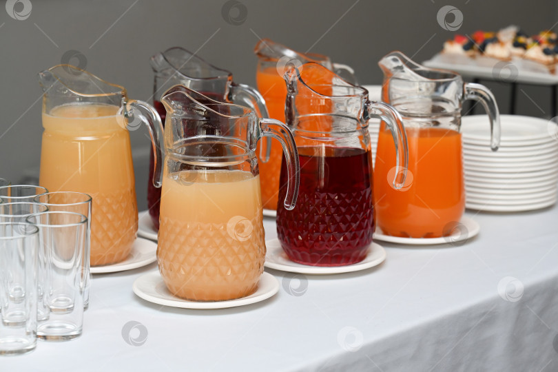 Скачать Стойка для напитков в формате ассорти с фруктовыми соками и ягодными морсами в стеклянных кувшинах на фуршетном столе для малолюдного мероприятия и местом для копирования меню фотосток Ozero