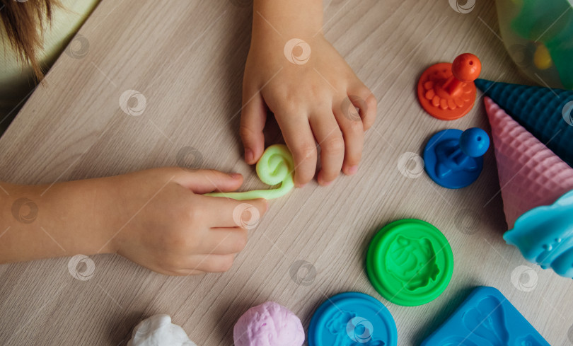 Скачать Маленькая девочка лепит фигурки из цветного воздушного пластилина, теста для лепки. Увлечения для детского творчества, развивающие занятия, развитие мелкой моторики рук. фотосток Ozero