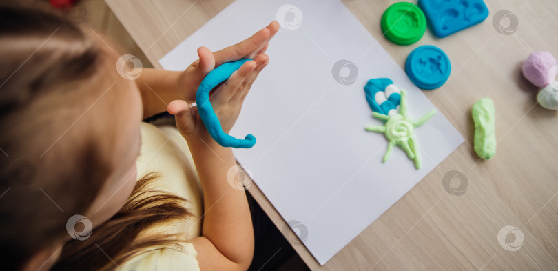 Скачать Маленькая девочка лепит фигурки из цветного воздушного пластилина, теста для лепки. Увлечения для детского творчества, развивающие занятия, развитие мелкой моторики рук. фотосток Ozero