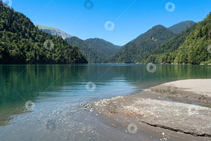 Скачать Чистое озеро Рица, окруженное горами, под ярко-голубым небом в летний сезон фотосток Ozero