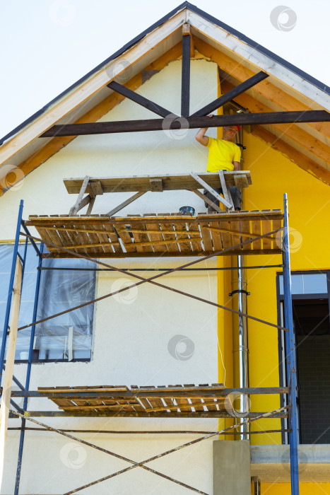 Скачать Застройщик осматривает завершенную конструкцию деревянного фронтона, опоры на внешних строительных лесах, современный желтый фасад, достижение мастерства, риск по высоте. фотосток Ozero