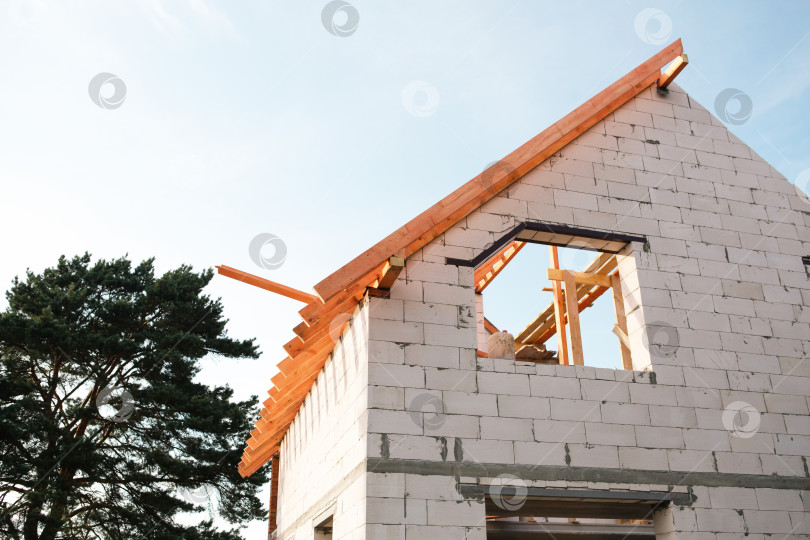 Скачать Современный белый блочный дом на этапе крепления стропил крыши, видна разметка деревянных лаг, кредит использован для строительства дома, финансовая безопасность за счет страхования. фотосток Ozero