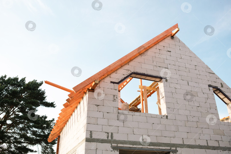 Скачать Вид спереди на дом на стадии активного строительства крыши, продолжается монтаж лаг, современный европейский стиль, строительство застраховано с привлечением ипотечного финансирования. фотосток Ozero