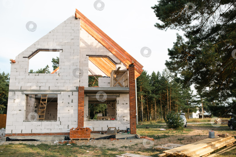 Скачать Новый евро-коттедж на стадии укладки кровли, классические окна, каменная кладка, конструкция крыши завершена с помощью ипотеки и застрахована по строительному полису. фотосток Ozero