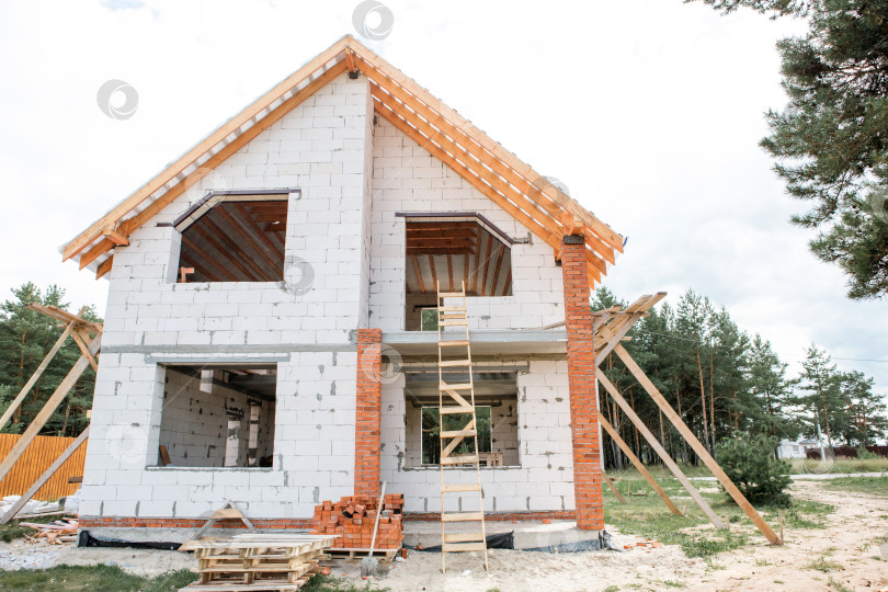 Скачать Современный дом с открытой стропильной системой, ведется монтаж лаг на крыше, светлый фасад, европейский архитектурный стиль, активное строительство. фотосток Ozero