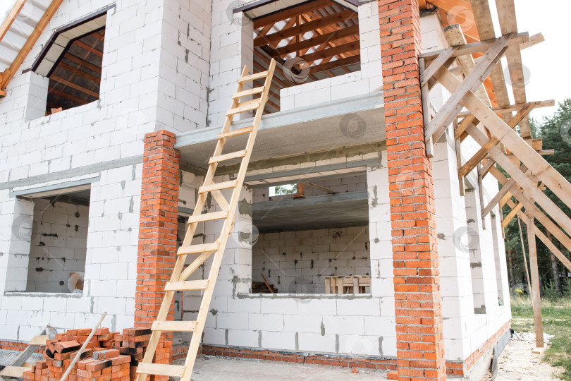 Скачать Крупный план кирпичного и газобетонного дома, рабочие монтируют каркас крыши, отчетливо видны лаги стропил, европейский метод строительства. фотосток Ozero