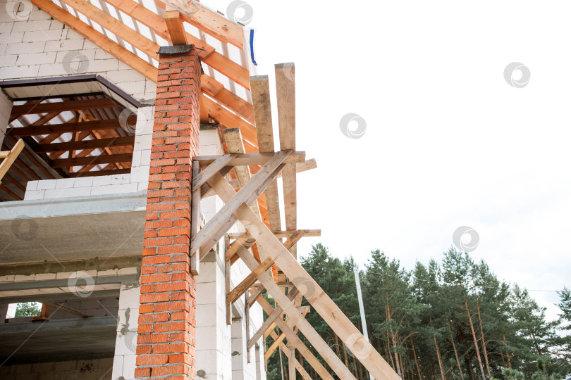 Скачать Дом европейской постройки, вид угловой стены и открытой стропильной рамы, продолжается установка лаг на крыше, видны строительные леса. фотосток Ozero