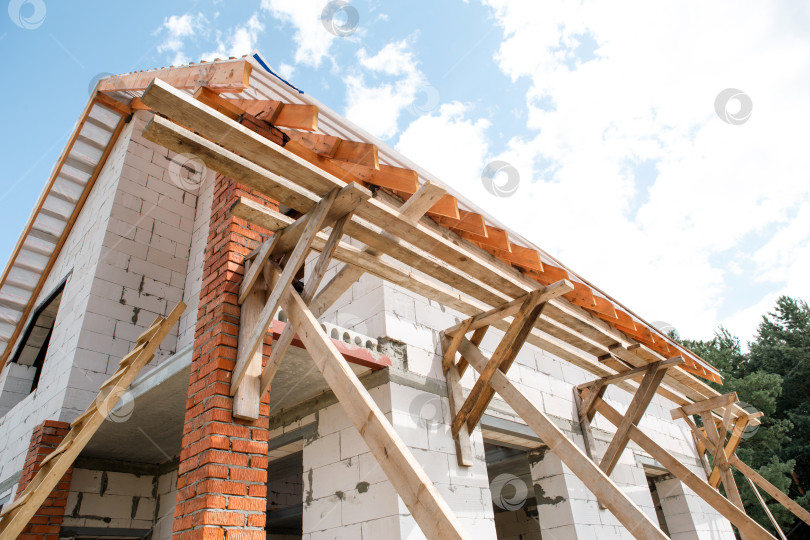 Скачать Большой строящийся дом, деревянная стропильная система и лаги образуют каркас крыши в евростиле, светлый фасад, работы продолжаются. фотосток Ozero