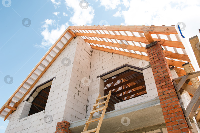 Скачать Дом в европейском стиле крупным планом, открытый каркас крыши с креплениями для стропил и лаг, видны строительные материалы и инструменты, продолжается монтаж крыши. фотосток Ozero