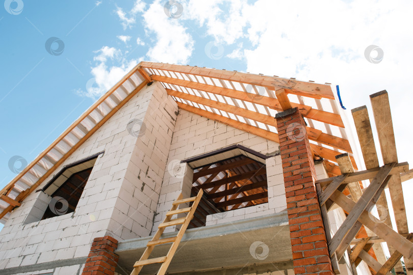 Скачать Современный блочный дом с деревянными лагами и фермами крыши, активная фаза монтажа кровельной конструкции, светлый отделанный кирпич. фотосток Ozero