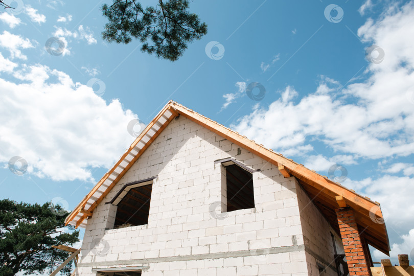Скачать Современный дом под голубым небом, видны лаги стропил и собранная стропильная конструкция, европейский стиль строительства, четко виден каркас кровли. фотосток Ozero