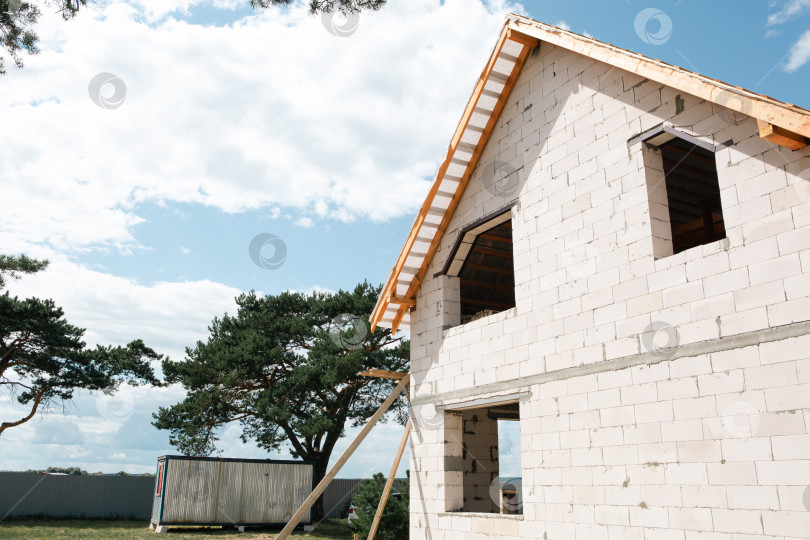 Скачать Перспективный вид нового дома во время монтажа кровельной системы, фермы и лаги формируют современный силуэт в евростиле, стены из кирпича и белых блоков. фотосток Ozero