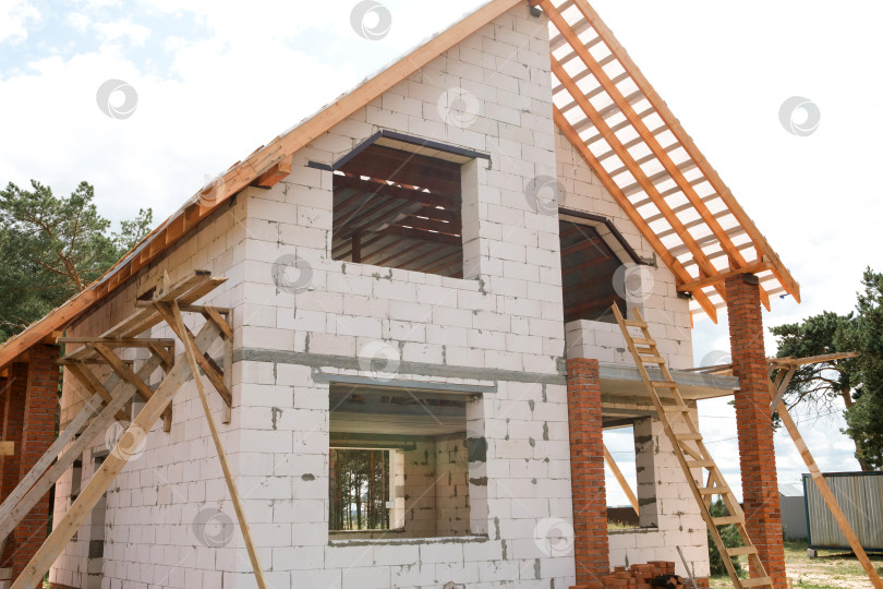 Скачать Здание из белых блоков и красного кирпича, смонтирована деревянная стропильная система, в классическом и современном гибридном стиле, виден монтаж лаг на крыше. фотосток Ozero