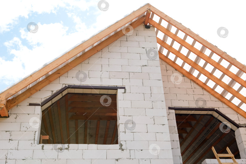 Скачать Современный дом на активной стадии строительства каркаса крыши, угловые деревянные лаги и опоры смонтированы на классической стене из блоков, детали в евростиле. фотосток Ozero
