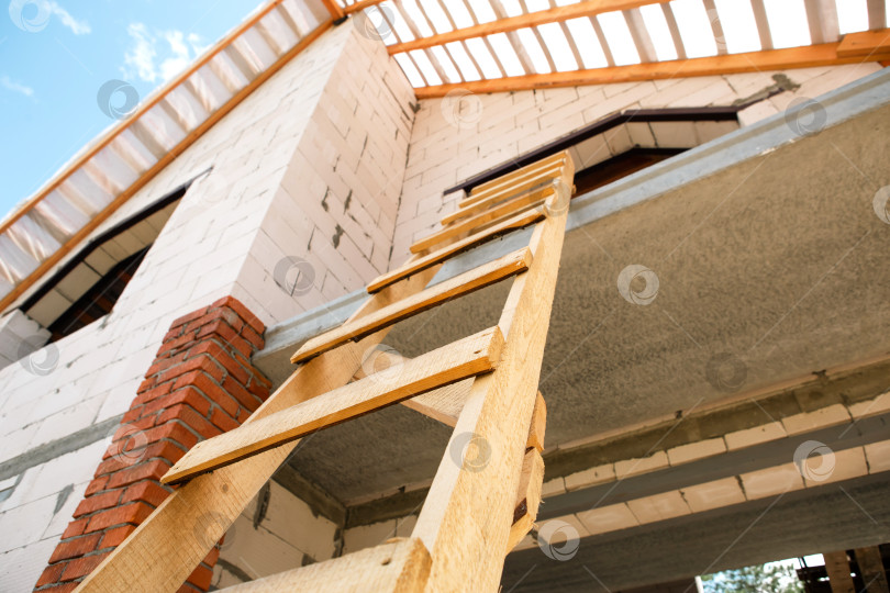 Скачать Нижний угол обзора крупным планом, современный кирпичный дом, видна система стропил и соединения лаг, продолжается поэтапное строительство крыши, европейское влияние. фотосток Ozero