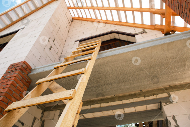 Скачать Современный дом, частично возведены строительные леса, завершен каркас мансарды и деревянные лаги крыши, внешняя отделка в европейском стиле, технология строительства. фотосток Ozero