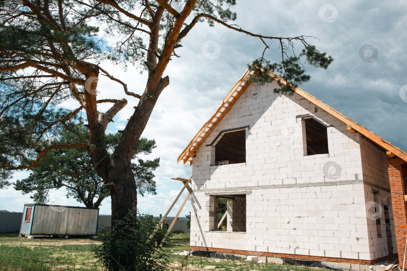 Скачать Белый современный дом с крышей в европейском стиле и системой stropil, строительство которого близится к завершению, классический внешний вид, строительная площадка, чистые линии. фотосток Ozero