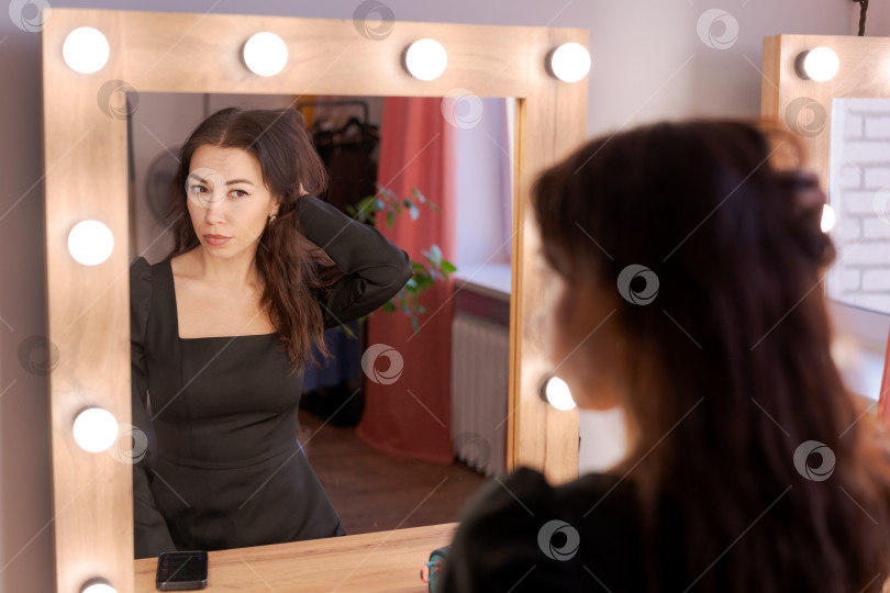 Скачать Женщина укладывает волосы перед зеркалом туалетного столика с лампочками фотосток Ozero