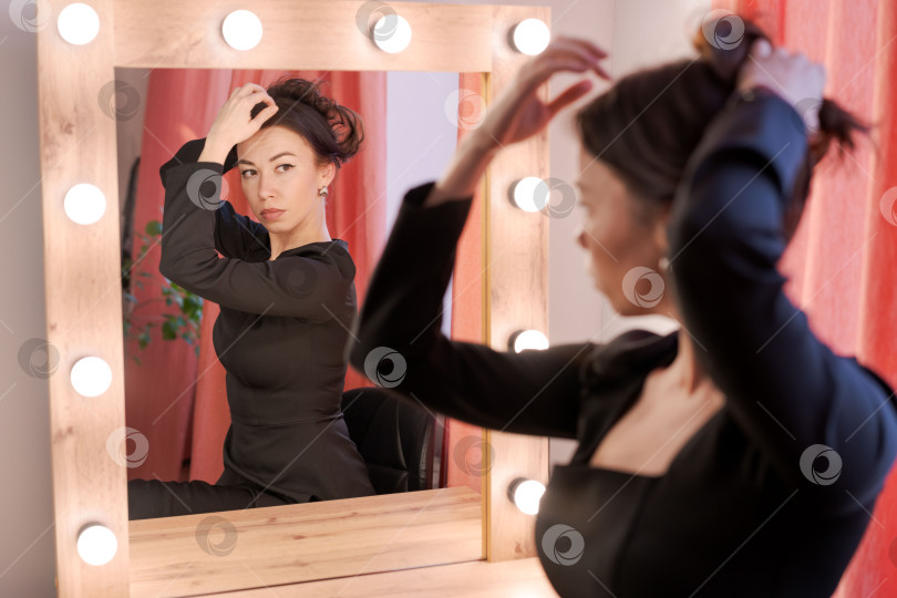 Скачать Женщина делает пучок для волос перед зеркалом туалетного столика с подсветкой фотосток Ozero