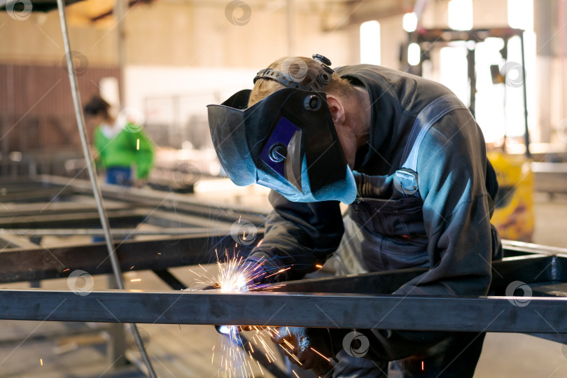 Скачать Сварщик в защитной маске Сваривает стальную конструкцию искрами фотосток Ozero