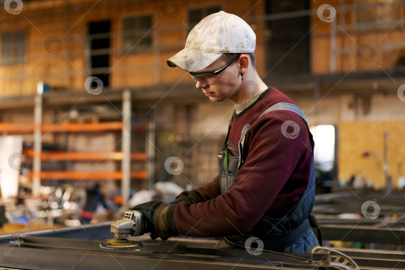 Скачать Молодой рабочий в защитных очках использует угловую шлифовальную машину на заводе фотосток Ozero