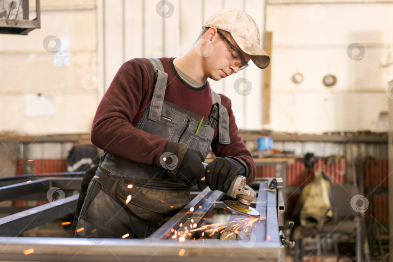Скачать Молодой промышленный рабочий использует шлифовальную машину на стальной конструкции фотосток Ozero
