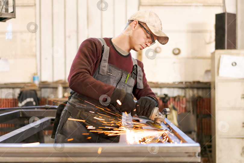 Скачать Молодой заводской рабочий шлифует сталь угловой шлифовальной машиной фотосток Ozero