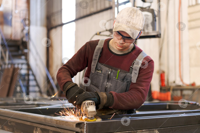 Скачать Молодой подмастерье использует угловую шлифовальную машину в слесарной мастерской фотосток Ozero