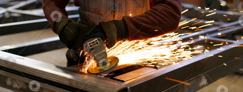 Скачать Рабочий по изготовлению металлоконструкций шлифует стальную раму с яркими искрами фотосток Ozero