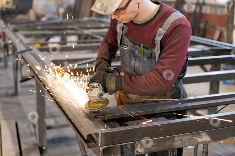 Скачать Молодой мастер, работающий углошлифовальной машиной на стальной конструкции фотосток Ozero