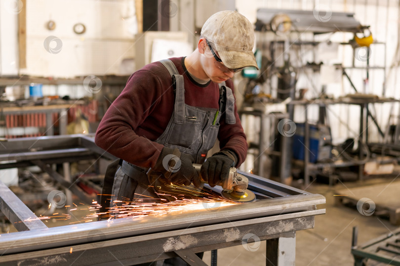 Скачать Молодой рабочий по металлу шлифует стальную раму в промышленном цехе фотосток Ozero
