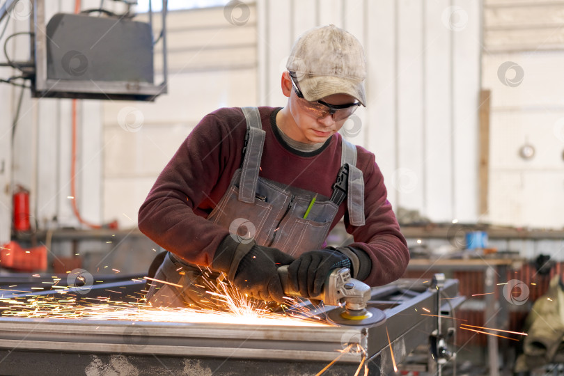 Скачать Молодой подмастерье шлифует металлическую раму с искрами на фабрике фотосток Ozero
