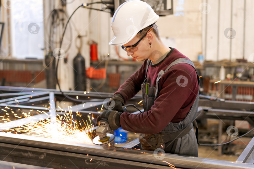Скачать Молодой рабочий в белой каске, высекающий искры из металла фотосток Ozero