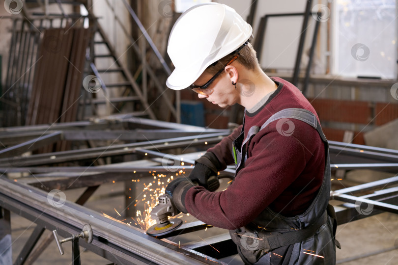Скачать Молодой подмастерье в каске для шлифования стальных конструкций фотосток Ozero