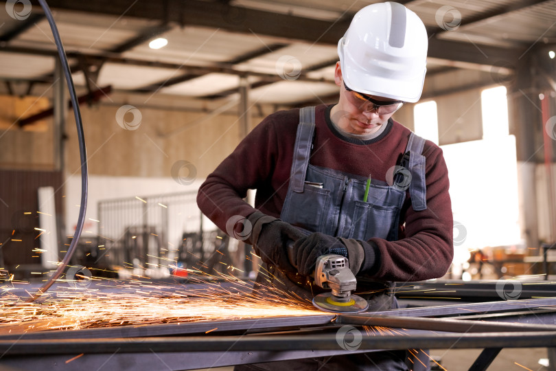 Скачать Молодой рабочий-металлист, шлифующий сталь в светлом заводском цехе фотосток Ozero