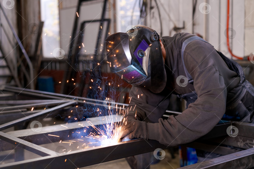 Скачать Сварщик в защитной маске Сваривает стальную раму искрами фотосток Ozero