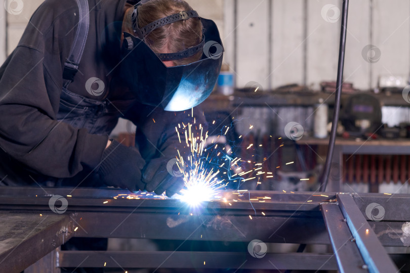 Скачать Старший сварщик, выполняющий сварку стальной рамы при ярком дуговом освещении фотосток Ozero