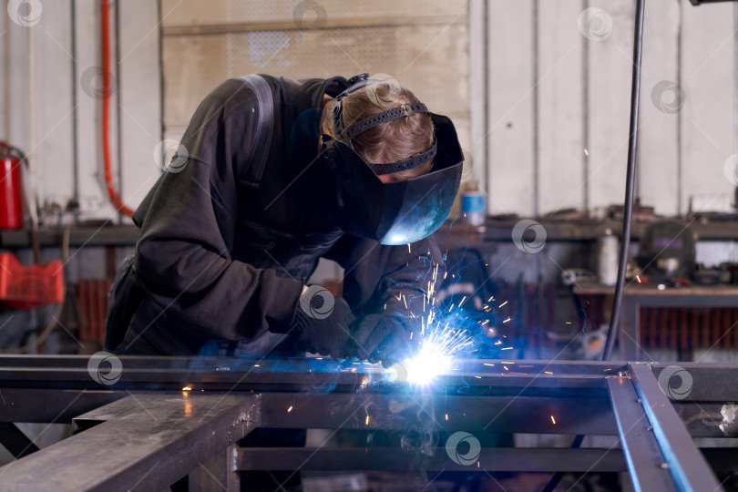 Скачать Старший сварщик, работающий на стальной раме с синей дуговой лампой фотосток Ozero
