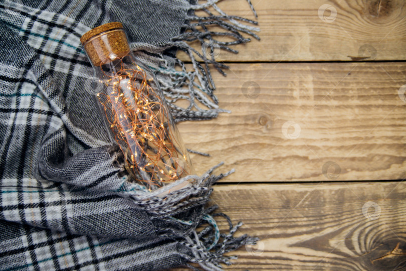 Скачать Гирлянда из рождественских огней в стеклянной бутылке.Теплый серый шарф или плед на деревянном фоне. фотосток Ozero