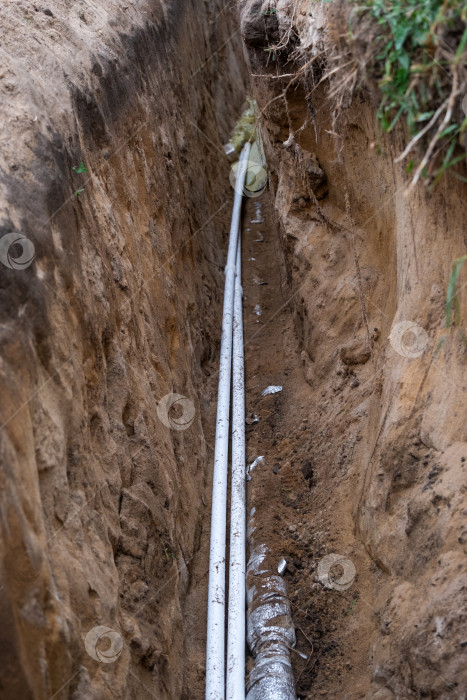Скачать Изолированная водопроводная труба в земляной траншее, прокладка под землей, инженерные коммуникации, земляные работы на участке, защита водопровода, рытье канала, покрытие грунтом, ремонт. фотосток Ozero