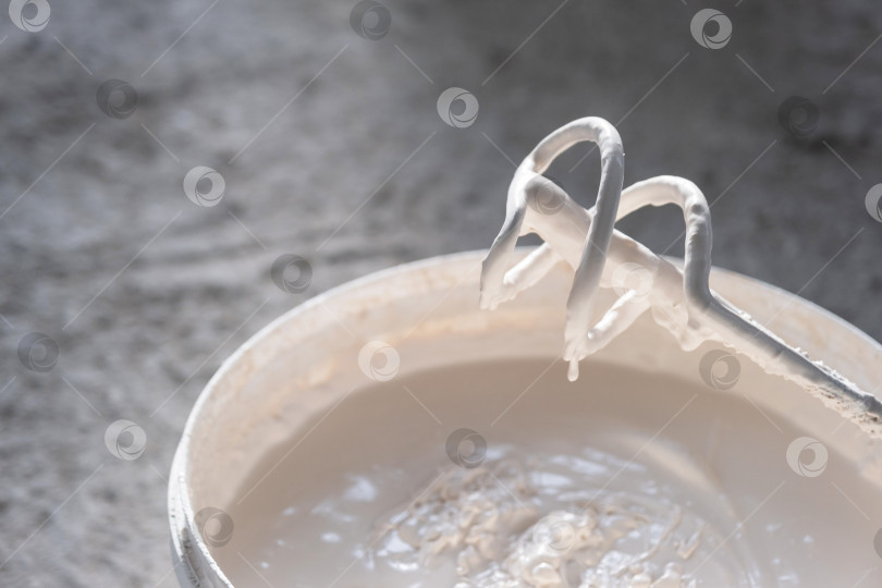 Скачать Замазка для ремонта стен, лопатка электрического миксера в строительном ведре, готова к оштукатуриванию, благоустройству дома, проверке консистенции, отделочному процессу. фотосток Ozero