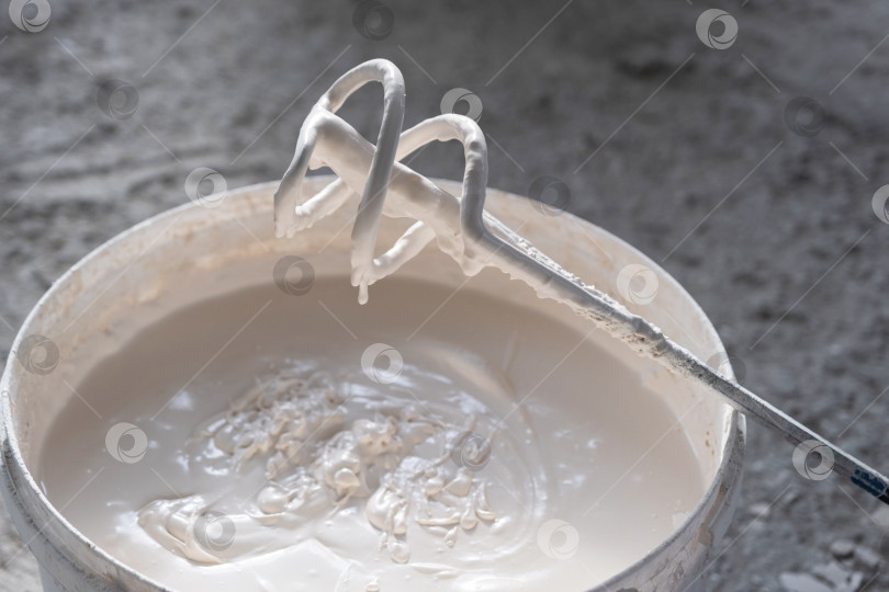 Скачать Приготовление штукатурной смеси с помощью электрического миксера, равномерное перемешивание шпаклевки, этап реконструкции, ремонтные работы, инструменты для отделки здания. фотосток Ozero