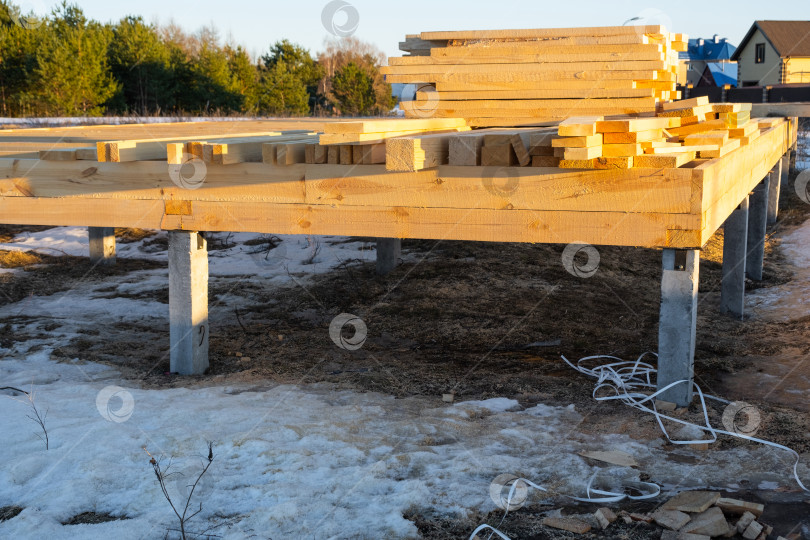 Скачать Пиломатериалы и балки для деревянного дома, укладываемые у фундамента, подготовка строительной площадки, строительство из бруса, столярные принадлежности, строительный инвентарь, начало проекта. фотосток Ozero