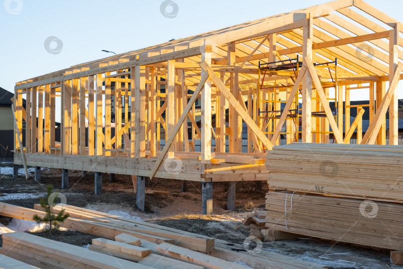 Скачать Строящийся деревянный каркасный дом, деревянный каркас, сборка балок, внешний вид, столярный проект, монтаж фундамента, наружная деревянная конструкция, установка опор. фотосток Ozero