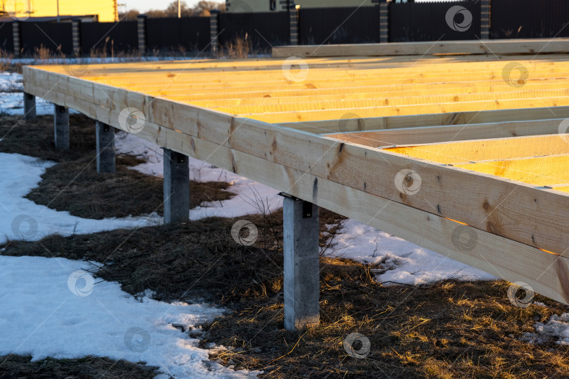 Скачать Вид фундамента на винтовых сваях, деревянной платформы и опорных балок, этап строительства каркасного дома, место проведения земляных работ, подготовка, монтаж подконструкции, установка опор. фотосток Ozero