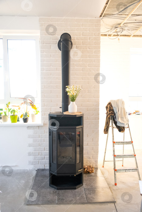 Скачать Установленная дровяная печь-камин в новом доме на этапе строительства, установленная на специальном основании для очага, установка и подготовка отопления дома. фотосток Ozero
