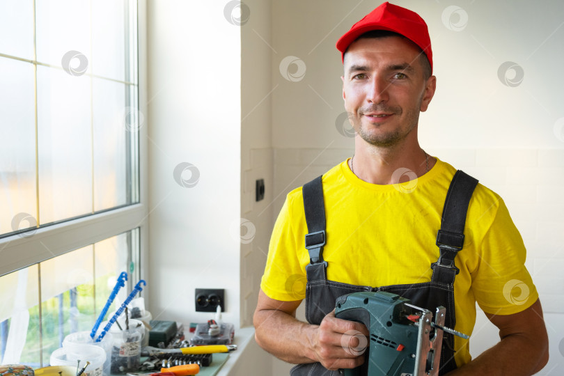 Скачать Портрет строителя в рабочей одежде, малярные валики и сверлильные инструменты, услуги разнорабочего, ремонтные работы, ремонт дома, выезд специалиста на дом, строительный бизнес. фотосток Ozero