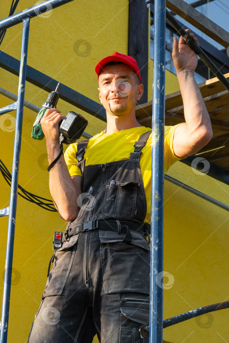 Скачать Мастер на все руки с малярным валиком и электроинструментом, строительные леса для ремонта дома, ремонт наружных стен, полный комплекс услуг по вызову, выезд мастера для консультации. фотосток Ozero