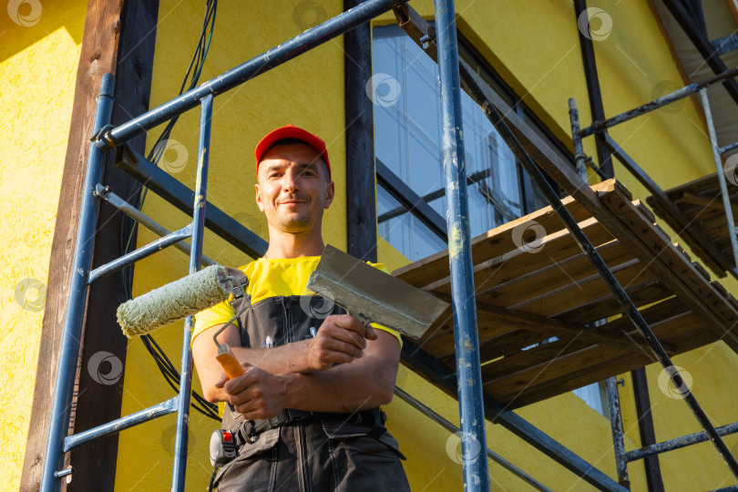 Скачать Портрет улыбающегося строителя, малярный валик, покраска фасадов, техническое обслуживание, услуги по ремонту дома, лестница, благоустройство, команда профессионалов, звонок клиенту, набор инструментов. фотосток Ozero